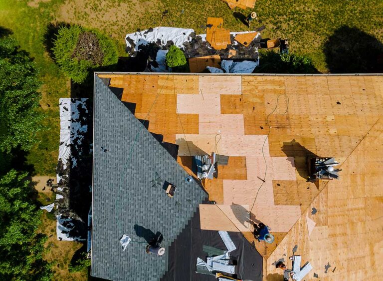 A large tree branch resting on a home’s shingled roof after a windstorm.