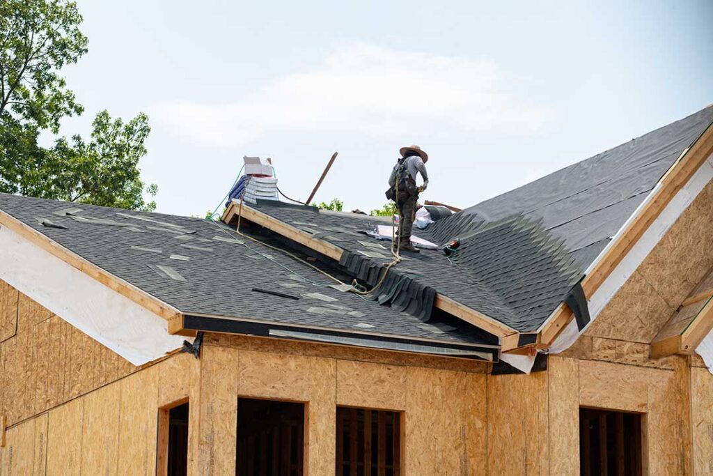 Person placing a bucket beneath a ceiling drip while moving furniture away from the wet area.