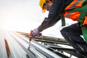 A person inspecting metal flashing around a roof vent beside overlapping shingles on a residential roof.