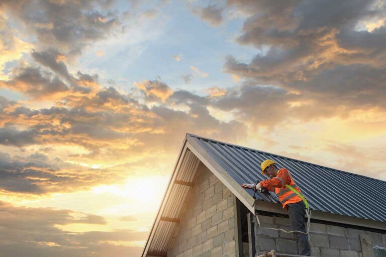 Person inspecting a shingle roof from the ground beside a ladder and leaf-covered gutters.