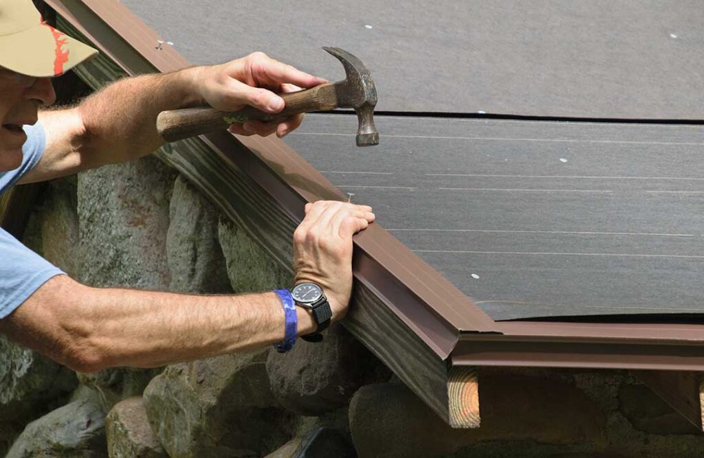 Person inspecting a residential roof from a ladder while checking gutters and shingles on a clear autumn day.