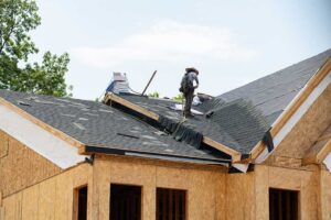 Homeowner reviews an insurance policy beside roof damage photos, receipts, and a flashlight on a kitchen table.