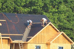 Person inspecting loose shingles and flashing beside a damp attic roof deck.