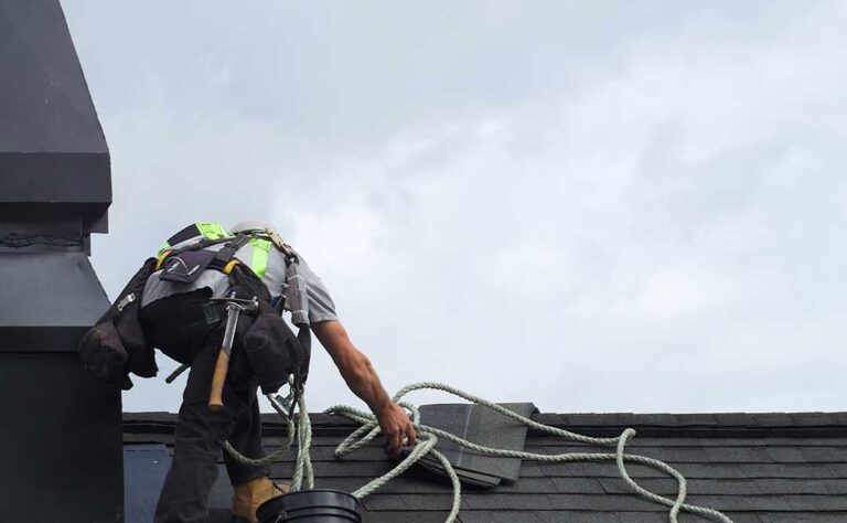 Homeowner reviews a roofing contract beside roof damage photographs and a calculator at a kitchen table.