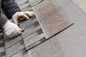 Close view of curled and cracked asphalt shingles on a residential roof beside a gutter.