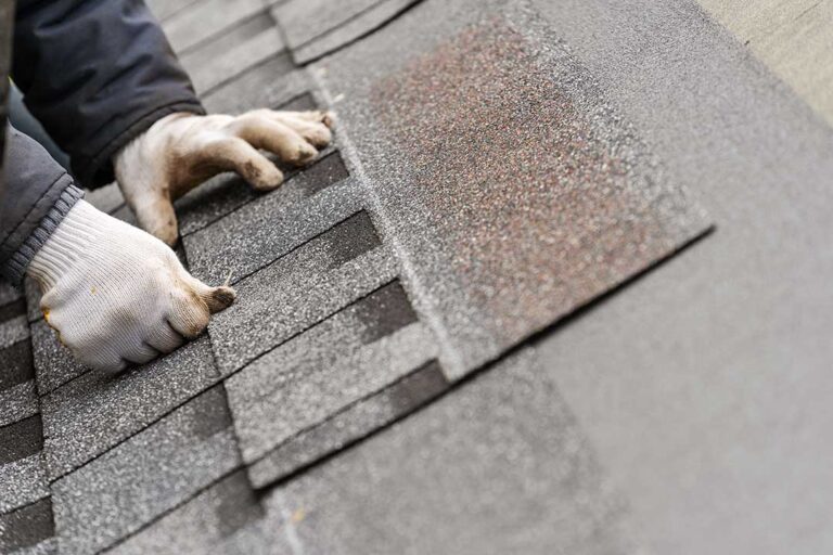 Close view of curled and cracked asphalt shingles on a residential roof beside a gutter.