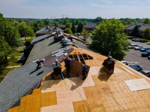Building inspector reviewing roof plans beside a winter home with shingles, flashing, and snow visible.